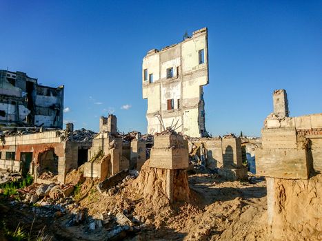 The ruins of a large destroyed building, pieces of stone, concrete, clay and metal against the blue clear sky