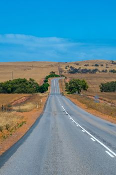 Australian bush road leading through dry landscape and farmland with empty road