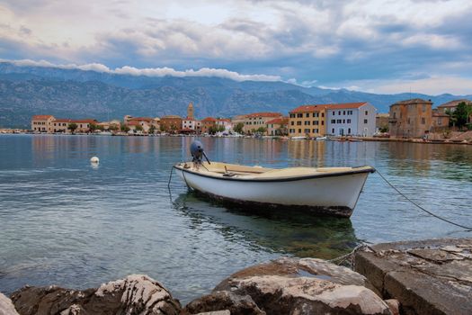 Traditional old village Vinjerac, Croatia, Velebit mountains and Paklenica national park in background, dramatic sky clouds, small fishing boat with engine in front
