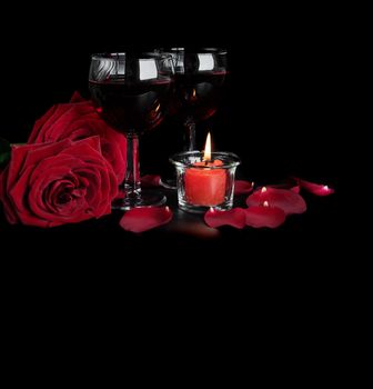Valentine's Days concept: two glasses of red wine, two red roses and a burning red candle isolated on a black background