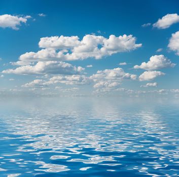 Vast blue summer sky with fluffy white cumulus clouds reflected in a water surface with small waves