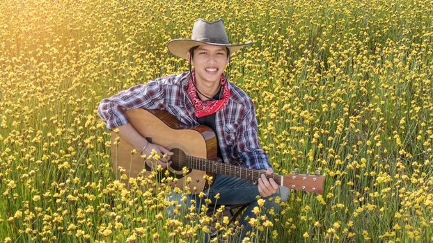 Asian farmer sitting in his bright yellow field with guitar