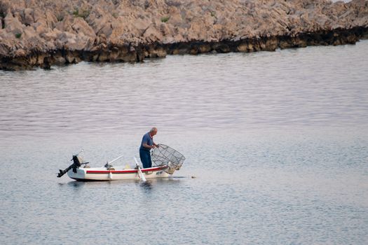 Old traditional fisherman in Croatia on a small wooden boat catching fish with fishing cage, pod, the catch is small due overfishing and makes a hard living the traditional way, unstaged, authentic
