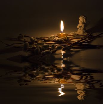Angel, burning candle and willow twigs reflected in the water surface with small waves