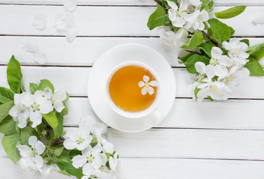 White cup of green tea and branches of apple-tree flowers on an old wooden shabby background