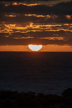 Sun just touching the horizon partly covered by red shining clouds during sunset in Australia
