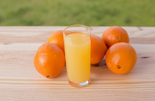 glass of delicious orange juice and oranges on table in garden