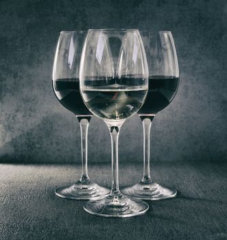 one glass white wine in front of two glasses red wine