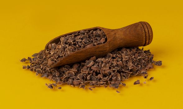 Grated chocolate. Pile of ground chocolate in wooden scoop isolated on yellow color background with clipping path, closeup