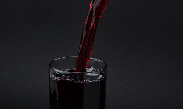 Cherry juice pouring into glass, isolated on black background, with copy space