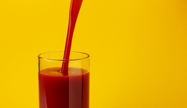 Tomato juice pouring into glass, isolated on yellow color background, with copy space, healthy drink concept, close-up