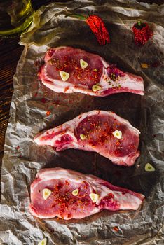 Three Raw Pork Steaks with Spices on Parchment Paper. Vertical.