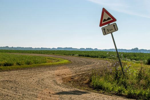 Road sign in countryside. Summer landscape with rural road, wood and cloudy blue sky. Classic rural landscape in Latvia. 

