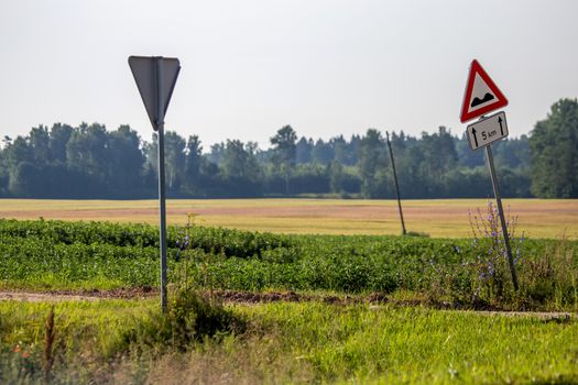 Road signs in countryside. Summer landscape with rural road, wood and cloudy blue sky. Classic rural landscape in Latvia. 

