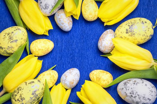 Happy Easter. Yellow fresh tulips lie on a blue background with Easter eggs.Happy Easter.