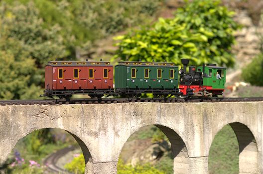 Model of locomotive pushing carriges on a concrete viaduct bridge. Garden model train.