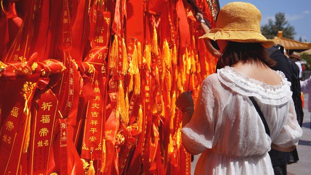 Two international tourists looking and reading through several ribbons with wishes. Tourists tied a red ribbon, China