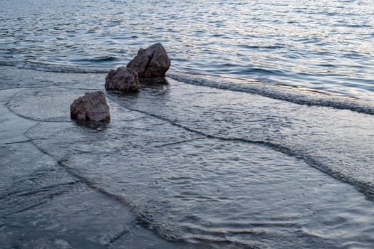 Small waves, ripples hitting beach with rocks in sunset, flushing over, three rocks in row overlapping, tranquil scene