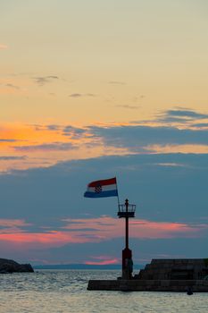 Cratian flag flying in wind at sunset in harbor, vertical composition, dusk after sundown, colorful clouds