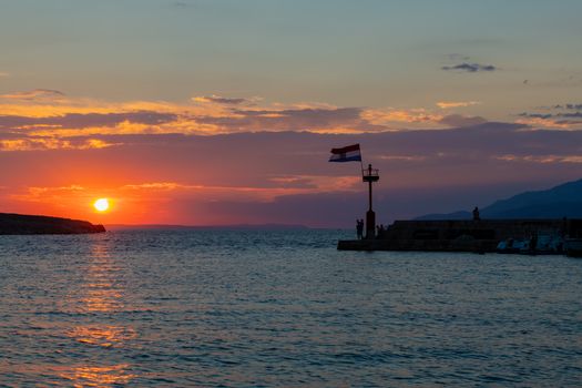 Croatian flag flying in wind at sunset in harbor, all people silhuetted and unrecognizable