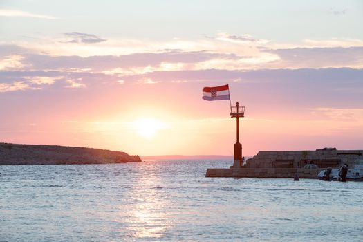 Croatian flag flying in wind at sunset in harbor, all people silhuetted and unrecognizable, bright scene, small boats in harbor