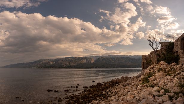 Ruins of stone house on waterfront in sunset, mountains and sea in background, Croatia, town of Vinjerac near Zadar, panorama, dramatic cloudscape above Velebit