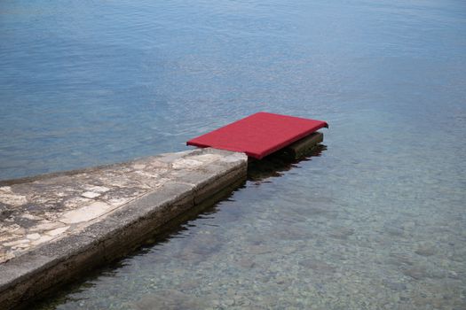 Stone pier with red carpet at waterfront, luxury beach vacation concept, welcome reception, travel
