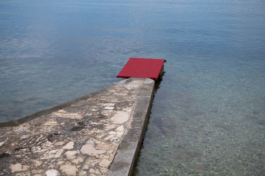 Stone pier with red carpet at waterfront, luxury beach vacation concept, guest treatment