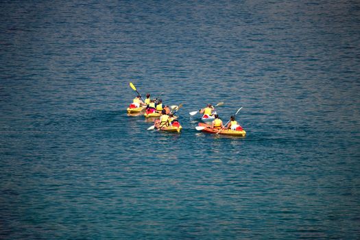 Mixed group of people, facing away, unrecogizable, canoeing at sea, vacation sport recreation, holiday outdoor activity