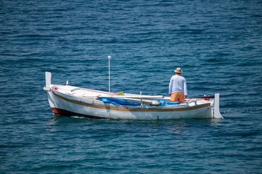 Fisherman in traditional wooden boat at sea, facing awaz from viewer, going out to sea, daylight, authentic and unstaged, mediterranean style, could be Italy, Greece, Croatia or Adriatic sea