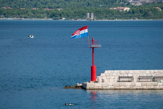 Croatian flag flying in wind on lighthouse in harbor, daytime, stone pier, nobody, patriotic concept