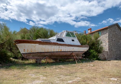 Abandoned boat on shore stone house in background, scene from traditional small fishing village in the Mediterranean, travel and vacation concept for tranquil places
