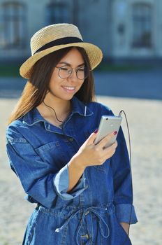 An attractive young Asian woman wearing sunglasses and a denim suit standing outside with a silver-colored phone
