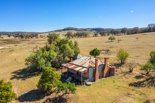 Run down old abandoned farm house with tin roof and bull nose verarandah.  The rear verandah has fallen down and its walls and floors warped and bulging.  Two chimneys one at the rear for a fire and cooking stove and the front  one for the main bedroom with mirror above it.  The starlings now fly in and out and the sheep make a home here too.