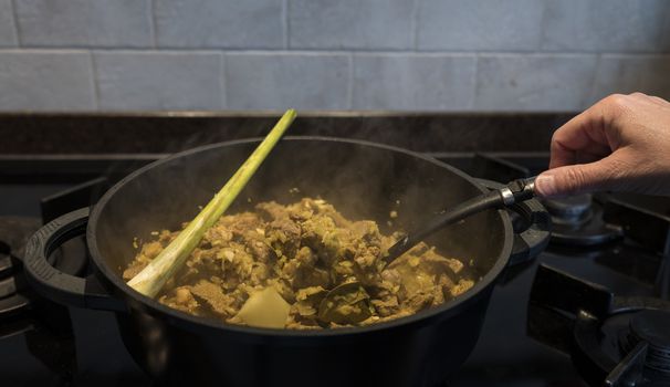 woman hand stirs in a pan on the gas stove with indonesian rendang, a stew with beef