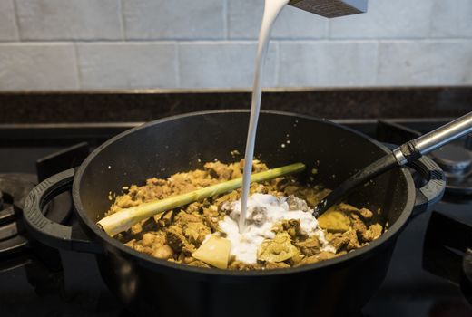 adding the coconut milk in a pan on the gas stove with indonesian rendang, a stew with beef