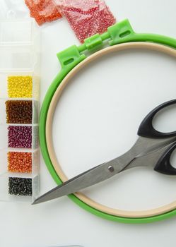 Flat lay needlework and embroidery accessories, scissors hoops and beads on white background, vertical frame.