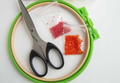 Flat lay needlework and embroidery accessories, scissors hoops and beads on white background,