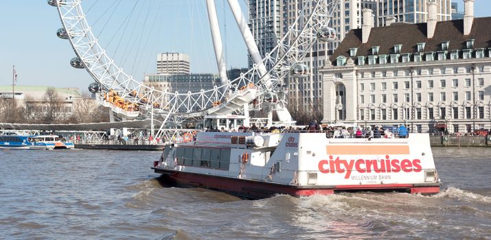 London, United Kingdom - Februari 21, 2019: A City cruises touristic boat navigating by Thames river with a lot of tourists on it, with London Eye in the background, in London, UK