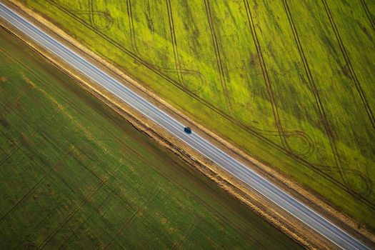 Aerial view of a car driving along a rural road between two fields