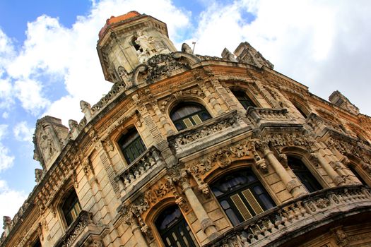 Facade of a beautiful building in Old Havana. The exterior of an old spanish-influence building. The Facade is made with rock and has several balconies. The windows is made of wood and the beautiful building has three levels.