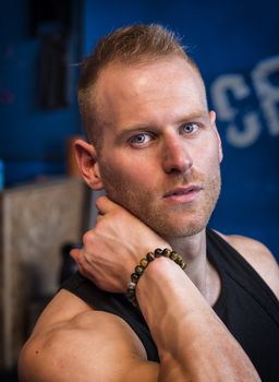 Attractive young man indoors wearing a tanktop and beaded bracelets