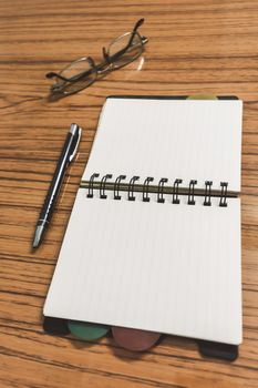 Desk with open notebook with blank pages, eye glasses and a pen. Business still life concept with office stuff on table. Education, working and planning concept. Selective focus with shallow DOF.