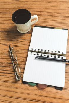 Desk with open notebook with blank pages, eye glasses, pen and a cup of coffee. Top view with copy space. Business still life concept with office stuff on table. Education, working or planning concept