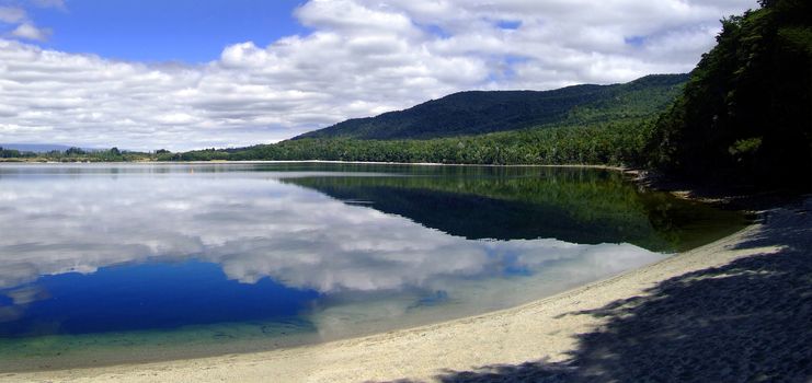 Lake Te Anau surface reflecting white clouds with blue sky and sandy beach. South island, New Zealand.