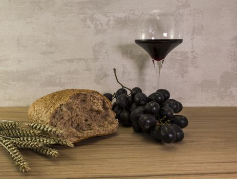 A wheat bread and shock of wheat with red grapes and glas of red wine as easter background