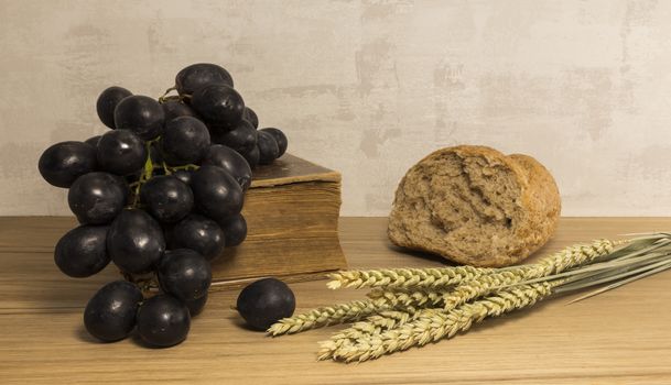 A wheat bread and shock of wheat with red grapes and and bible as easter background