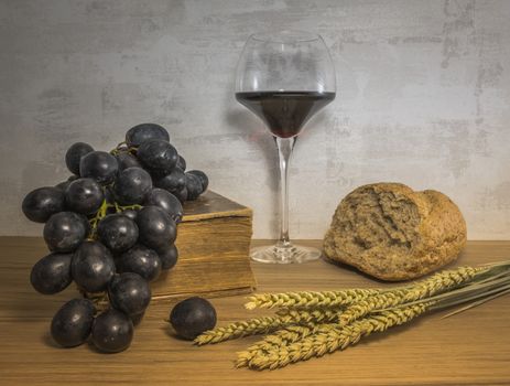 A wheat bread and shock of wheat with red grapes and glas of red wine and bible as easter background