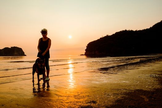 Senior Woman and dog on beach at sunrise