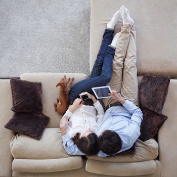 Couple using digital tablet at home sitting on sofa, top view